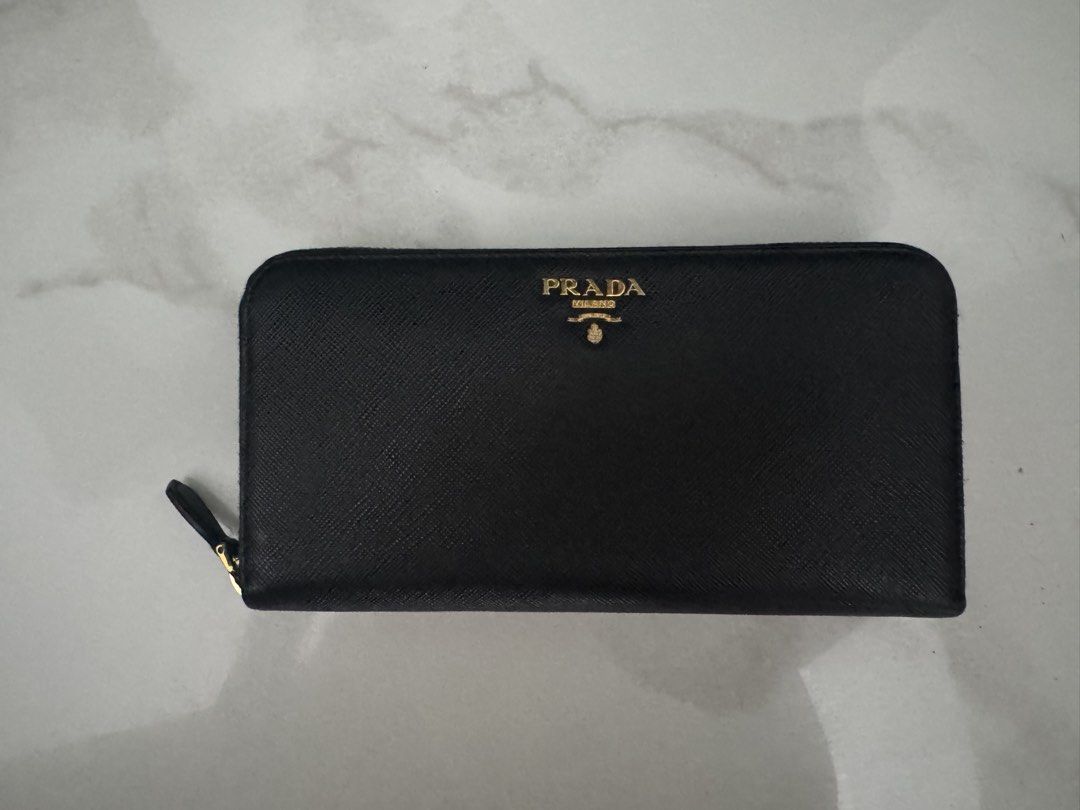 Prada Black Saffiano Leather Zip Around Wallet (Category: Luxury Bags & Wallets) located in Manila. Submitted by decluterthings888 (Listing ID 1470779523, Image 1). Description: - Authentic Prada zip-around wallet - Material: Premium black Saffiano leather - Hardware: Elegant gold-tone with metal lettering logo - Interior: Multiple card slots, slip compartments, and zippered coin pocket - Condition: Clean fabric lining, smooth working zipper - Pe