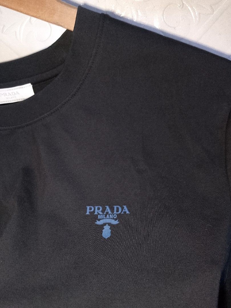 Prada Milano Black T-Shirt Size M (Category: Shirts) located in Manila. Submitted by mjthrifted_second (Listing ID 1470823934, Image 3). Description: - Brand: Prada Milano - Style: Crewneck short sleeve tee - Color: Solid black with blue embroidered chest logo - Size: Medium (Standard fit) -Dimes: 21/27 - Material: Premium cotton - Origin: Made in Italy - Authenticity: Interior neck label and wash tags intact (Style Code: UCS339) - Trusted Carous