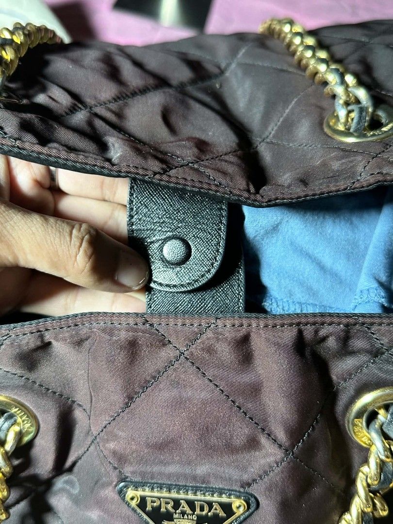 Prada Quilted Nylon Chain Tote Bag Brown (Category: Luxury Bags & Wallets) located in Naga. Submitted by mrwisethrifter (Listing ID 1470853957, Image 3). Description: - Brand: Prada - Material: Quilted nylon with Saffiano leather trim - Color: Brown with gold-tone hardware - Straps: Gold-tone chain interwoven with leather - Hardware: Iconic triangular Prada logo plaque on the front - Closure: Saffiano leather snap strap at the top - Interior: Bla
