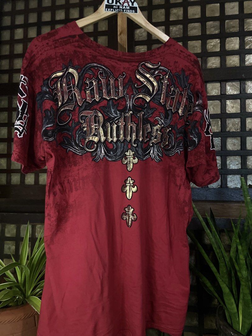 Raw State Graphic Skull T-Shirt Red (Category: Tshirts & Polo Shirts ) located in Nampicuan. Submitted by aireann_10 (Listing ID 1470861255, Image 2). Description: - Brand: Raw State - Color: Red - Size: Large - Design: Large skull with wings and scroll lettering on front; matching back print with three gold crosses - Fit: Short sleeves, crew neck - Style: Bold streetwear with heavy detailing.