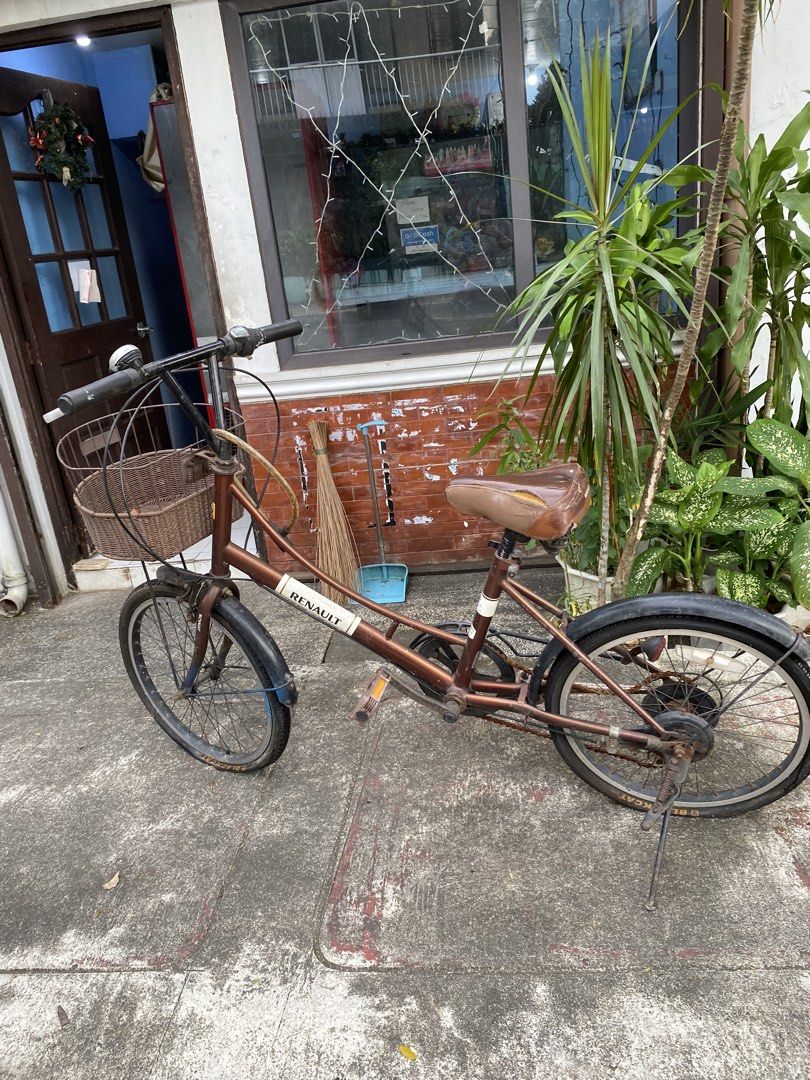 Renault City Bicycle With Basket (Category: Bicycles) located in Manila. Submitted by ziongavin0506 (Listing ID 1470818192, Image 1). Description: Renault brown city bike, step-through frame design. Front wicker-look storage basket included. Black handlebars with grip shifters and silver brake levers. Brown leatherette saddle has a rip on the side exposing foam. Chain and drivetrain show significant rust. Kickstand attached at the rear. Black tir