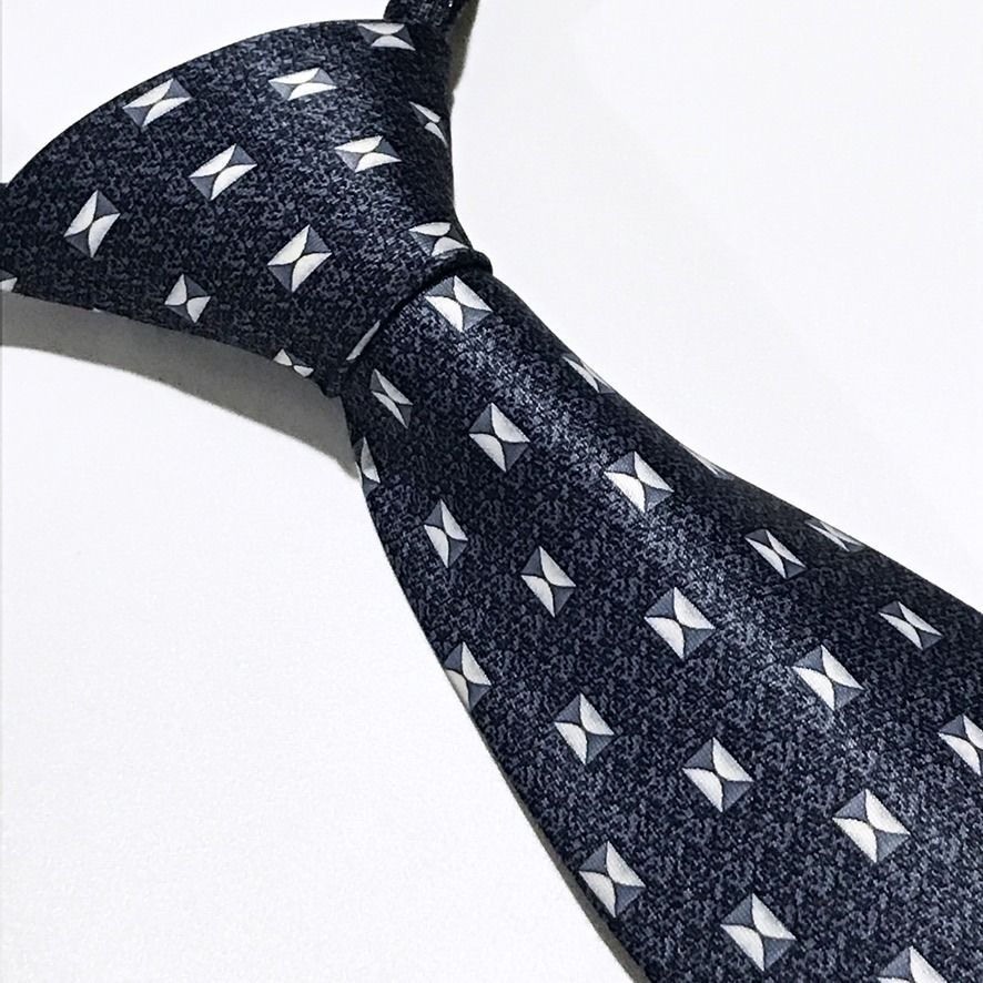 Rene Chagal Geometric Pattern Slate Blue Neck Tie (Category: Ties) located in Taguig. Submitted by retrogaze (Listing ID 1470851142, Image 1). Description: This necktie by Rene Chagal features a slate blue ground with a subtle, stippled micro-pattern. The body is decorated with an orderly geometric foulard pattern of small, square bowtie-like motifs rendered in crisp white, light grey, and charcoal accents. Recommended Suit & Shirt Pairings: • Th
