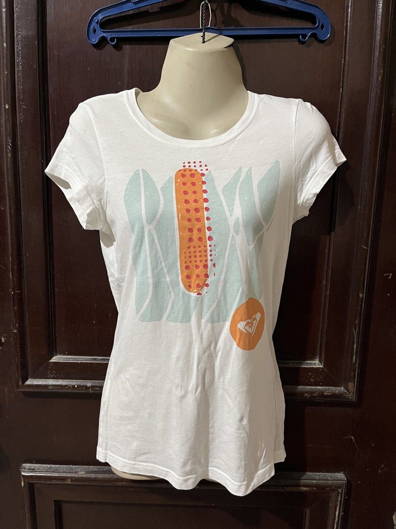 Roxy Graphic Print Short Sleeve T-Shirt (Category: Shirts) located in Siniloan. Submitted by marceiron316276 (Listing ID 1470848984, Image 1). Description: - Brand: Roxy - Color: White with turquoise and orange graphic print - Size: S - Material: Comfortable cotton feel - Design: Classic crew neck, short sleeves - Measurements: ~15.5" chest across, ~26.5" total length - Condition: Excellent.