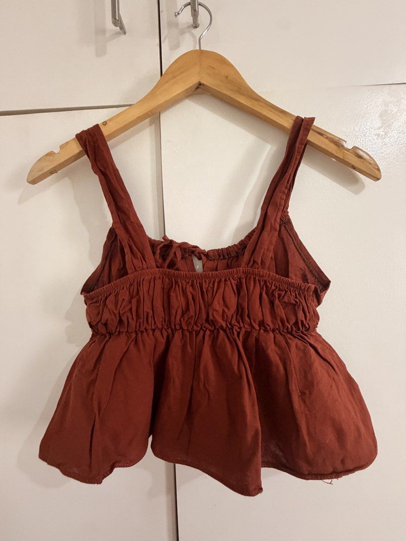 Rust red ruffled crop top with tie detail (Category: Sleeveless) located in Marikina City. Submitted by _bananahanaa (Listing ID 1470798919, Image 2). Description: - Color: Rust Red - Style: Crop top with flouncy peplum hem and gathered bodice - Details: Thick straps, front self-tie string, and elasticized back band for a secure fit - Fabric: Lightweight and breathable - Perfect for: Casual days out, best paired with high-waisted jeans - Conditio
