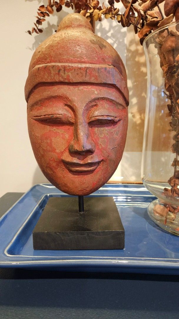 Rustic Smiling Wood Buddha Head Sculpture on Stand (Category: Wall Decor) located in Manila. Submitted by cosmicshark-cd31f1 (Listing ID 1470878621, Image 2). Description: - Hand-carved wooden Buddha head sculpture - Mounted on a sturdy black square metal stand - Distressed red and brown finish with visible wood grain and aging texture - Hollow backing showing traditional carving technique - Perfect unique tabletop decor for bookshelves or entryw