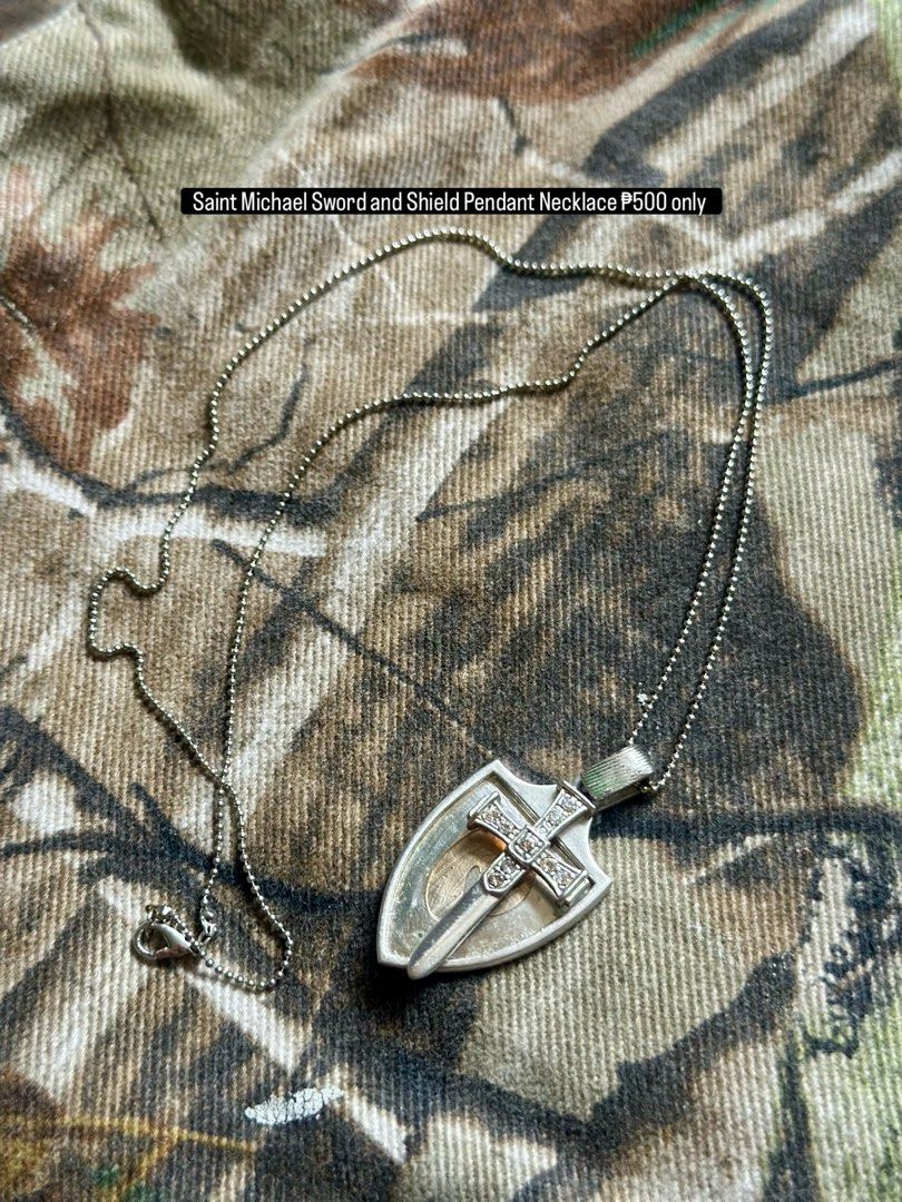 Saint Michael Sword and Shield Pendant Necklace (Category: Necklaces) located in Daet. Submitted by thrifthings2018 (Listing ID 1470751373, Image 1). Description: - Design: Silver-tone shield and sword with a rhinestone-embedded cross - Inclusion: Matching ball chain necklace with a secure clasp closure - Condition: Clean metal finish, ready to wear.