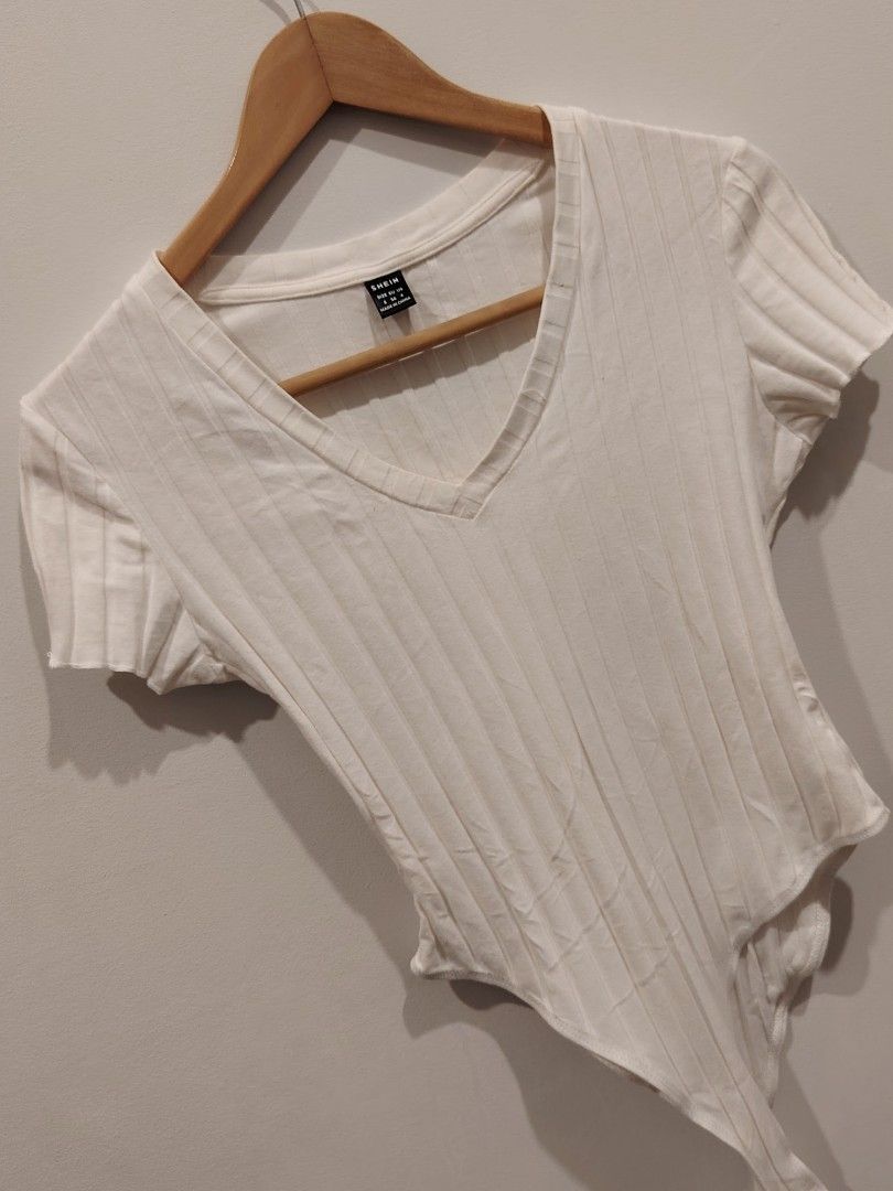 SHEIN White Ribbed V-Neck Bodysuit Size S (Category: Sleeveless) located in Manila. Submitted by jacelllamb12233 (Listing ID 1470859585, Image 1). Description: - Brand: SHEIN - Color: White with ribbed texture - Size: S (tag attached) - Design: Short sleeves, flattering V-neckline - Closure: Bottom snap buttons for easy wear - Material: Stretchy, comfortable fabric.