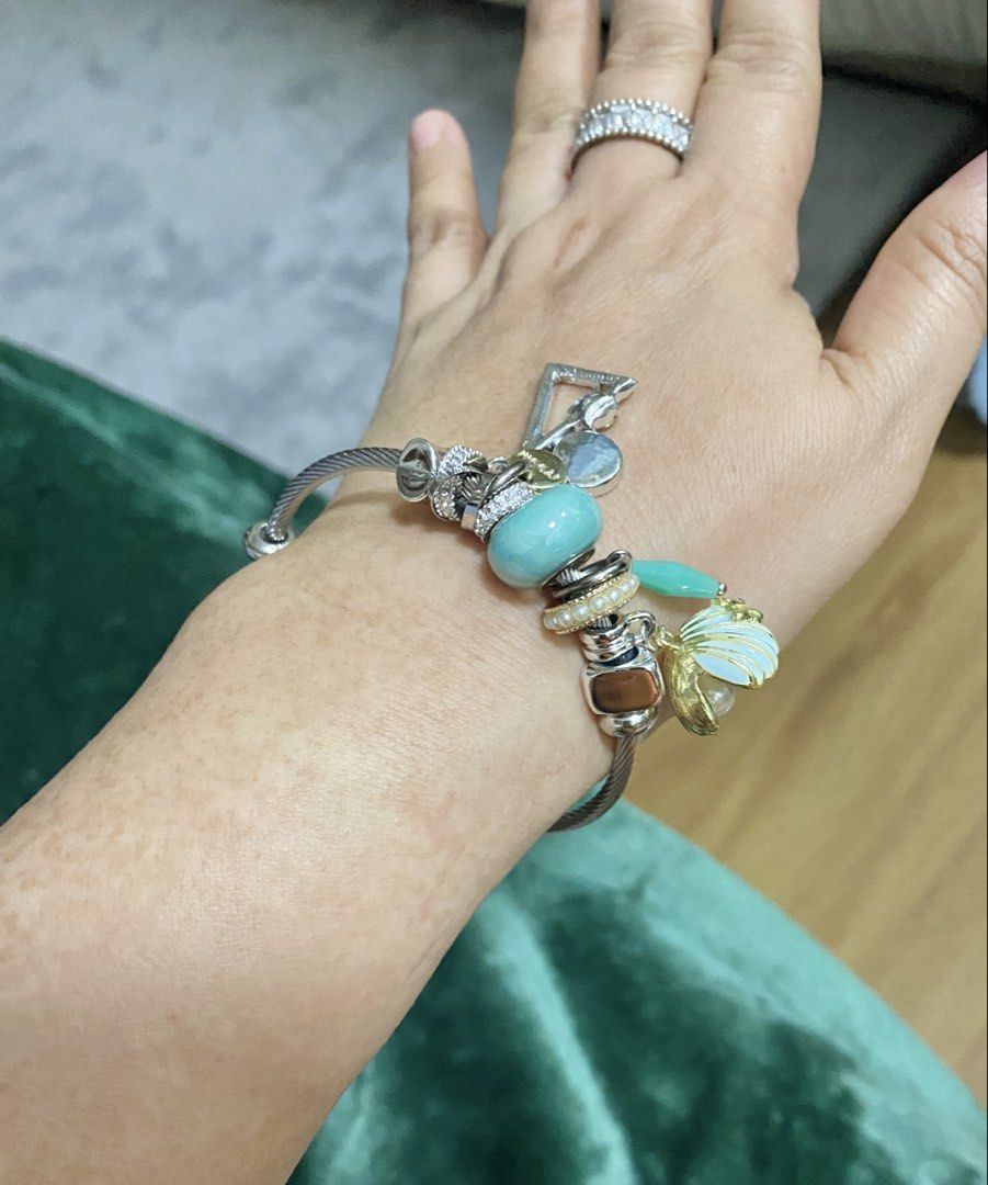 Silver Charm Bracelet with Turquoise and Shell Charms (Category: Bracelets) located in Makati City. Submitted by dpjanssen (Listing ID 1470867957, Image 1). Description: - Silver-tone cable bangle bracelet loaded with unique charms - Features a large turquoise bead, pearl ring spacer, geometric shape, teardrop stone, and gold-rimmed white shell dangle - Fits most wrist sizes comfortably - Metal shows minor wear near the ends.