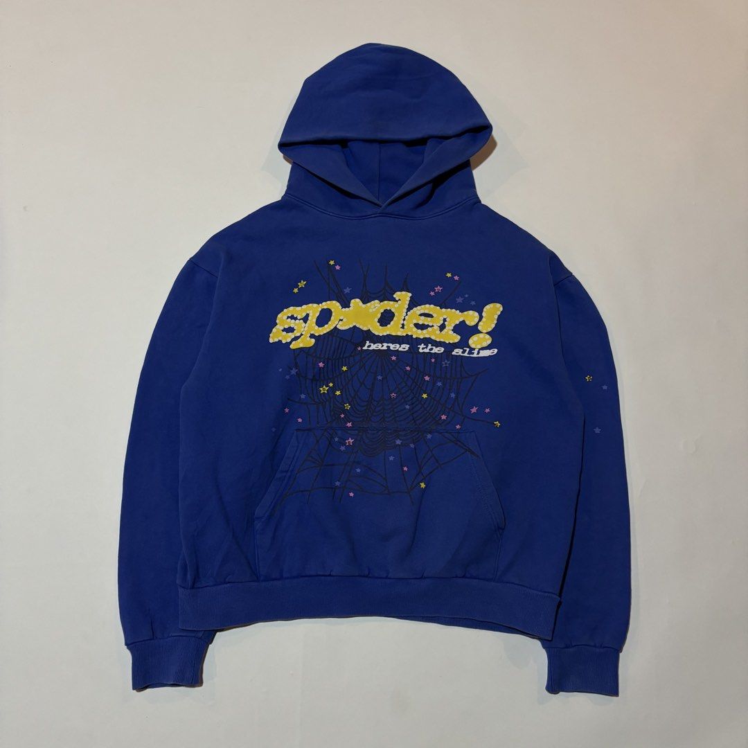 Sp5der Here's The Slime Blue Hoodie (Category: Coats, Jackets and Outerwear) located in Dipolog. Submitted by dionato (Listing ID 1470778399, Image 1). Description: - Color: Royal blue with yellow polka dot branding - Size: XL - Material: 100% thick cotton (Machine wash cold) - Design: Detailed spiderweb graphic on front and pocket with scattered colorful stars - Features: Cozy kangaroo pocket and thick hood - Condition: Brand new with printed ta