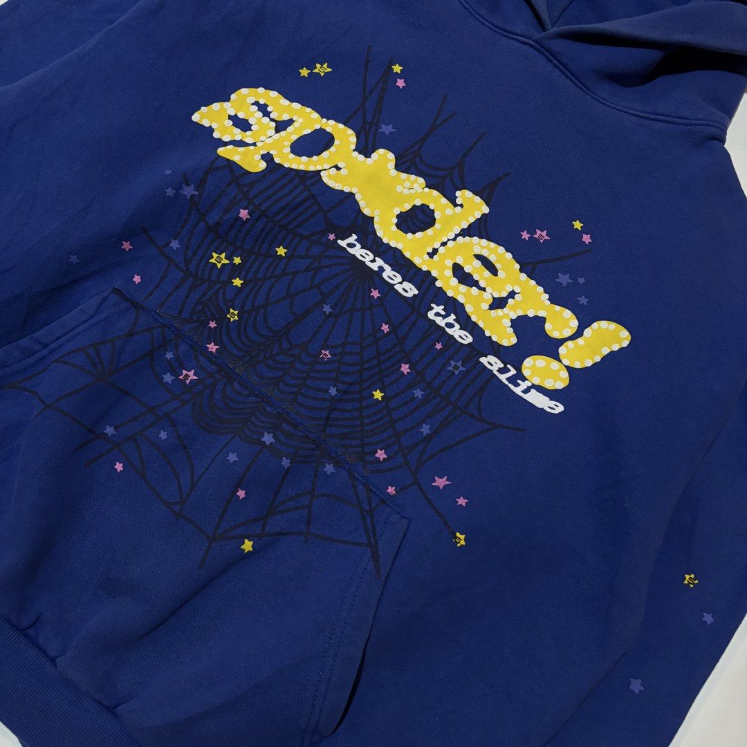 Sp5der Here's The Slime Blue Hoodie (Category: Coats, Jackets and Outerwear) located in Dipolog. Submitted by dionato (Listing ID 1470778399, Image 3). Description: - Color: Royal blue with yellow polka dot branding - Size: XL - Material: 100% thick cotton (Machine wash cold) - Design: Detailed spiderweb graphic on front and pocket with scattered colorful stars - Features: Cozy kangaroo pocket and thick hood - Condition: Brand new with printed ta