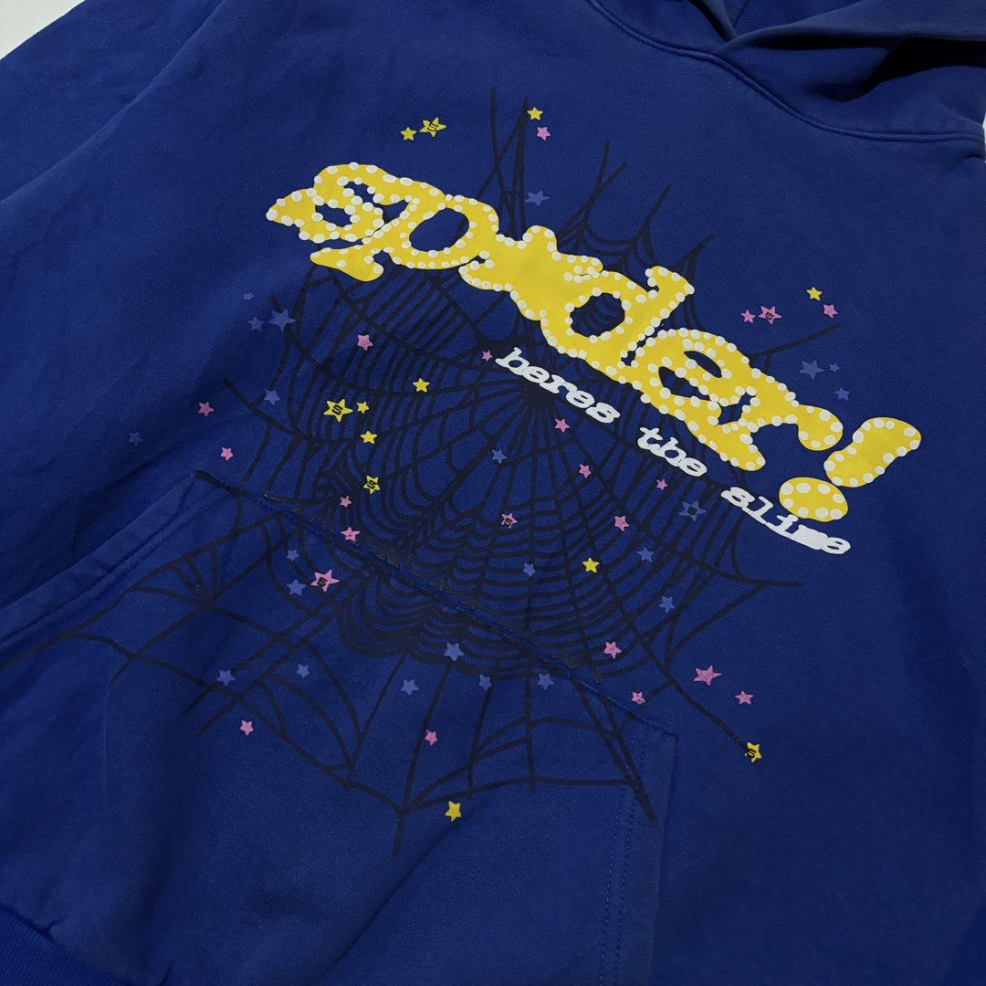 Sp5der Here's The Slime Blue Hoodie (Category: Coats, Jackets and Outerwear) located in Dipolog. Submitted by dionato (Listing ID 1470778399, Image 2). Description: - Color: Royal blue with yellow polka dot branding - Size: XL - Material: 100% thick cotton (Machine wash cold) - Design: Detailed spiderweb graphic on front and pocket with scattered colorful stars - Features: Cozy kangaroo pocket and thick hood - Condition: Brand new with printed ta