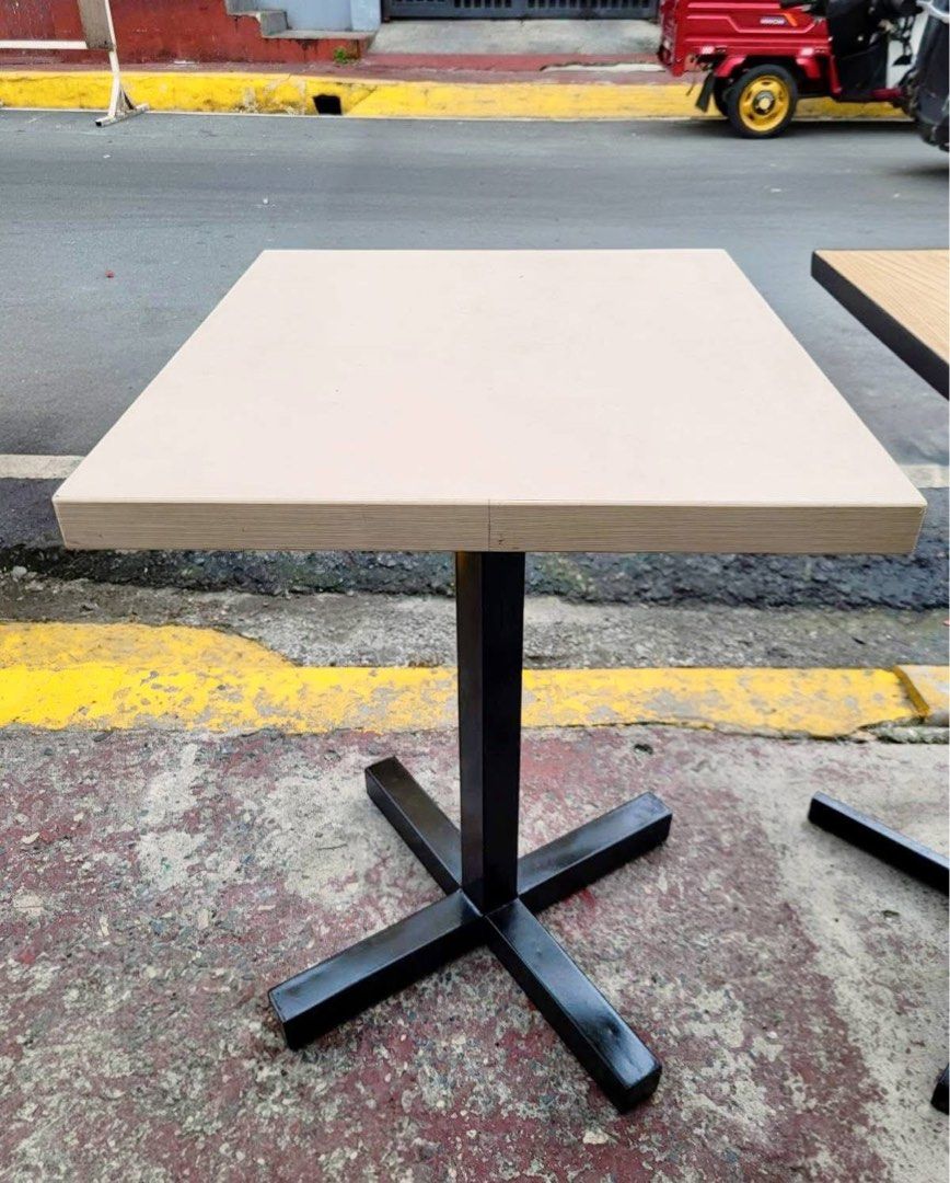 Square Restaurant Tables and Padded Cube Stools (Category: Tables & Sets) located in Manila. Submitted by jakeglads0 (Listing ID 1470745800, Image 1). Description: - Table: Square café table with light beige/natural wood finish and sturdy black metal cross base - Stools: Padded cube stools upholstered in durable faux leather - Colors: Assorted colors including grey, brown, red, maroon, and beige - Best for: Small dining spaces, coffee shops, and 