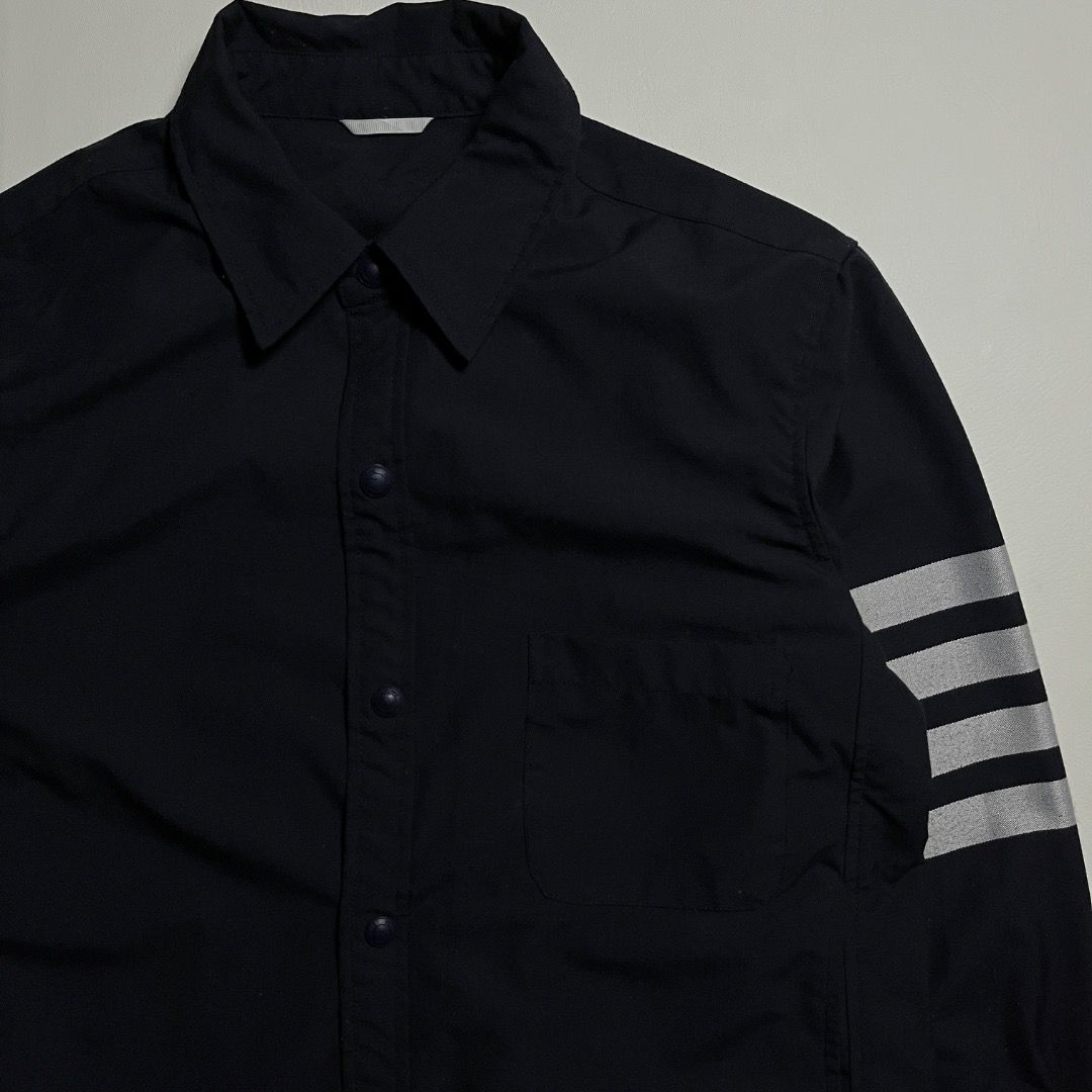 Thom Browne 4-Bar Long Sleeve Button Up Shirt (Category: Formal Shirts) located in Caloocan City. Submitted by achilles_grails (Listing ID 1470843999, Image 2). Description: - Brand: Thom Browne - Color: Dark Navy - Style: Smart casual button-up shirt with snap-button closure and classic tailoring - Signature Details: Four-bar stripes on left sleeve, front chest pocket with brand patch tag, and iconic tricolor grosgrain loop tab at back collar - 
