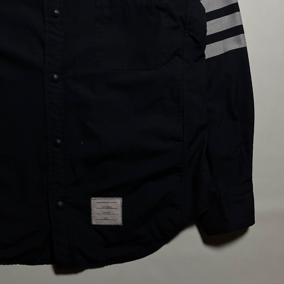Thom Browne 4-Bar Long Sleeve Button Up Shirt (Category: Formal Shirts) located in Caloocan City. Submitted by achilles_grails (Listing ID 1470843999, Image 3). Description: - Brand: Thom Browne - Color: Dark Navy - Style: Smart casual button-up shirt with snap-button closure and classic tailoring - Signature Details: Four-bar stripes on left sleeve, front chest pocket with brand patch tag, and iconic tricolor grosgrain loop tab at back collar - 
