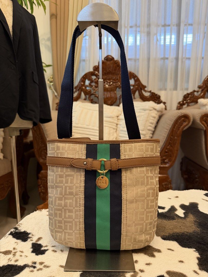 Tommy Hilfiger Monogram Canvas Shoulder Bag Navy Green (Category: Shoulder Bags) located in Santiago. Submitted by yrellagnoihsaf (Listing ID 1470764587, Image 1). Description: - Brand: Tommy Hilfiger - Material: Beige monogram canvas with dark navy straps - Design: Blue and green central stripe with decorative brown faux leather strap and gold-tone logo charm - Closure: Zip top - Interior: Dark navy lining with a red zipper pocket and Tommy Hilf