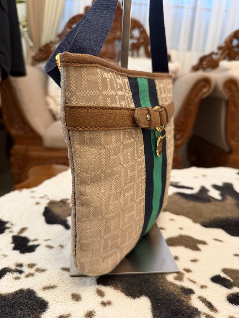 Tommy Hilfiger Monogram Canvas Shoulder Bag Navy Green (Category: Shoulder Bags) located in Santiago. Submitted by yrellagnoihsaf (Listing ID 1470764587, Image 3). Description: - Brand: Tommy Hilfiger - Material: Beige monogram canvas with dark navy straps - Design: Blue and green central stripe with decorative brown faux leather strap and gold-tone logo charm - Closure: Zip top - Interior: Dark navy lining with a red zipper pocket and Tommy Hilf