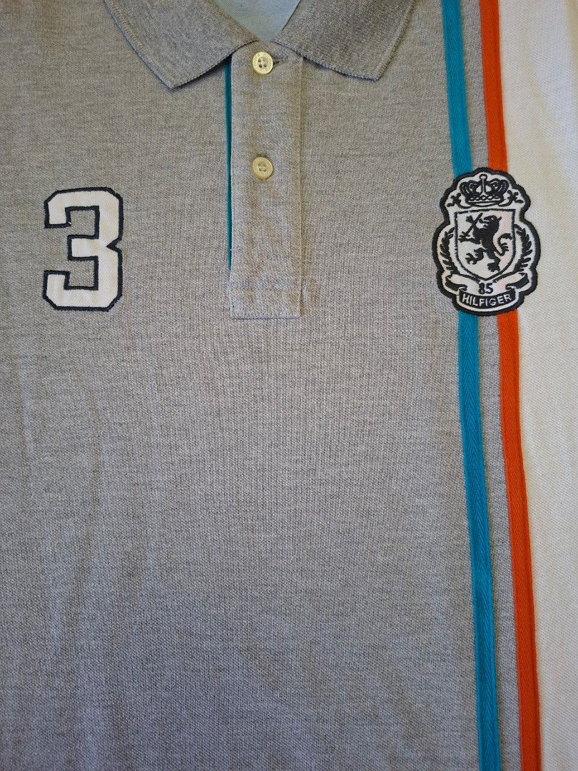 Tommy Hilfiger Polo Shirt (Category: Activewear) located in Rizal. Submitted by carou66859 (Listing ID 1470781832, Image 2). Description: This is a gray Tommy Hilfiger polo shirt featuring a number "3" patch on the right chest, a crest patch on the left chest, and vertical blue and orange racing stripes.Size 22 inches width and 29 inches length.An original, brand-new retail Tommy Hilfiger polo shirt featuring custom embroidery or crest accents ty