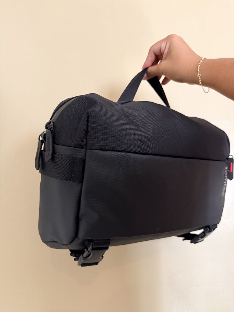 Tomtoc Black laptop Sling Bag (Category: Sling Bags) located in Paranaque City. Submitted by missb1001 (Listing ID 1470804460, Image 3). Description: - Brand: Tomtoc - Color: Solid black - Material: Durable cordura ballistic nylon with ykk zippers and pull tabs - Straps: Adjustable shoulder strap + exterior bottom buckle straps for jackets or extra gear - Pockets: Front zipped pocket with subtle branding - Condition: Clean interior lining, excell