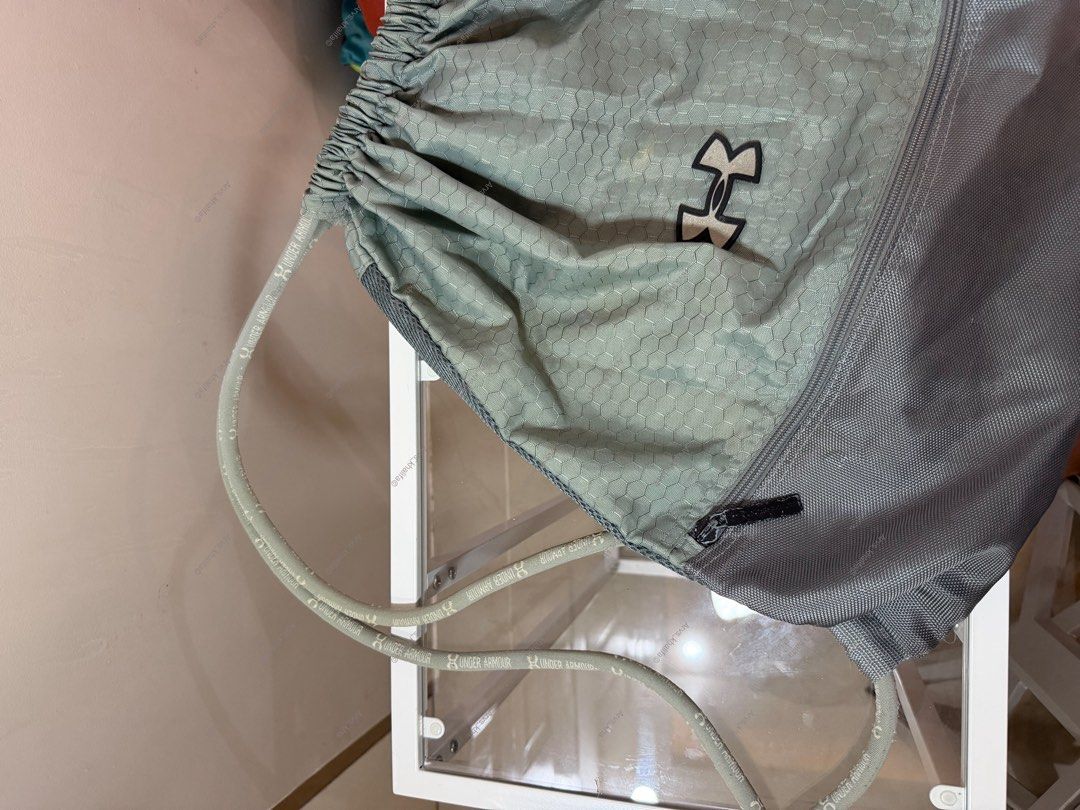 Under Armour Gym Sackpack Drawstring Bag Grey (Category: Backpacks) located in Rosario. Submitted by chippycoco (Listing ID 1470767329, Image 1). Description: - Authentic Under Armour drawstring bag in stylish sage green and grey - Unique hexagon pattern on the main body with a handy zippered side pocket - Thick, durable rope straps featuring the iconic Under Armour logo .