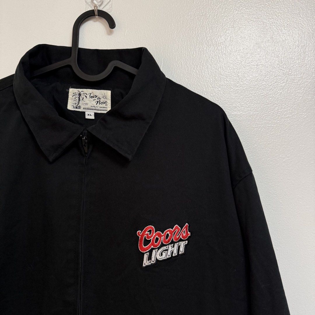 (Vintage) Coors Light Harrington Jacket (Category: Coats, Jackets and Outerwear) located in Orion. Submitted by whoknew.vtg (Listing ID 1470754705, Image 1). Description: (Vintage) Black Coors Light “Toes on the Nose” Harringtong Jacket Zip Up Size : XL Dimes : W26 L31.5 .