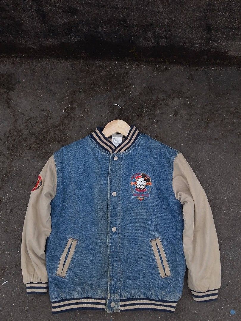 Vintage Mickey Mouse Denim Varsity Jacket (Category: Coats, Jackets and Outerwear) located in Baler. Submitted by vansonearth (Listing ID 1470752212, Image 1). Description: - Classic denim varsity jacket with Mickey Mouse graphics (front & back) - Cream-colored sleeves with ribbed striped cuffs, collar, and hem - Snap button front closure with slanted waist pockets - 1928 heritage design - Casual streetwear style, ideal for layering in colder wea