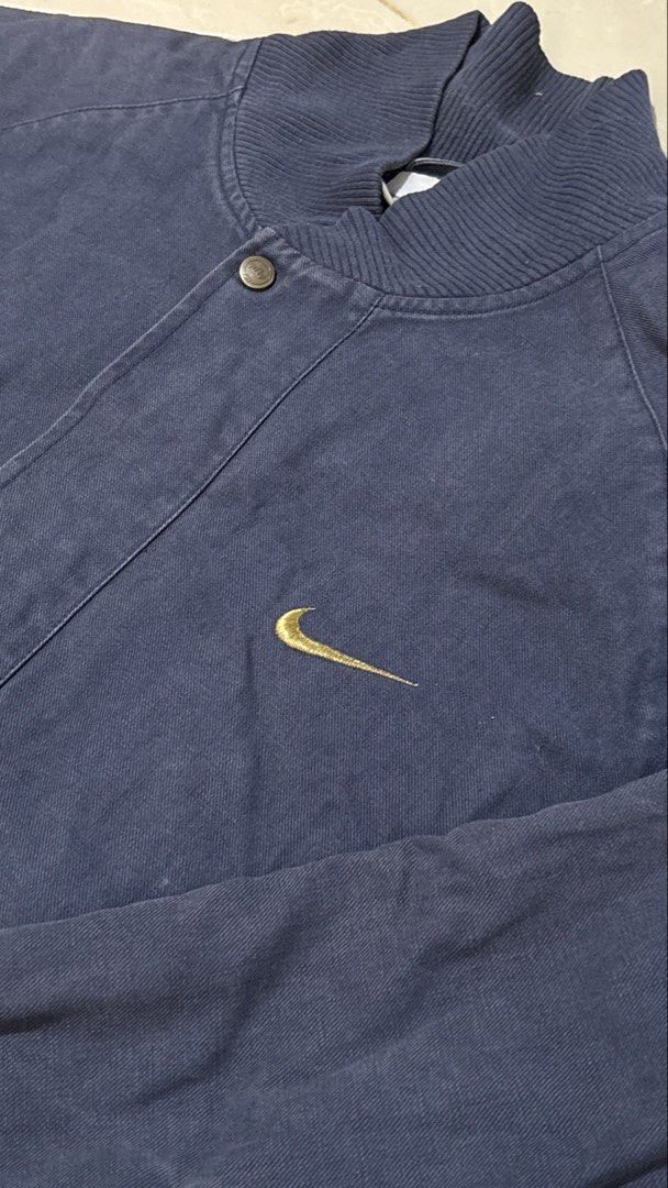 Vintage Nike Navy Blue Varsity Bomber Jacket (Category: Coats, Jackets and Outerwear) located in Manila. Submitted by glano (Listing ID 1470862658, Image 3). Description: - Brand: Nike - Style: Retro varsity jacket - Color: Dark navy blue with white and gold accents - Details: Gold embroidered swoosh on chest, large white Nike graphic on back - Trim: Ribbed collar, cuffs, and hem with white and gold stripes - Hardware: Full zip closure and custom