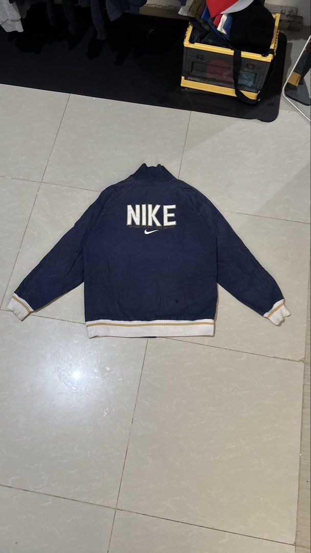Vintage Nike Navy Blue Varsity Bomber Jacket (Category: Coats, Jackets and Outerwear) located in Manila. Submitted by glano (Listing ID 1470862658, Image 2). Description: - Brand: Nike - Style: Retro varsity jacket - Color: Dark navy blue with white and gold accents - Details: Gold embroidered swoosh on chest, large white Nike graphic on back - Trim: Ribbed collar, cuffs, and hem with white and gold stripes - Hardware: Full zip closure and custom