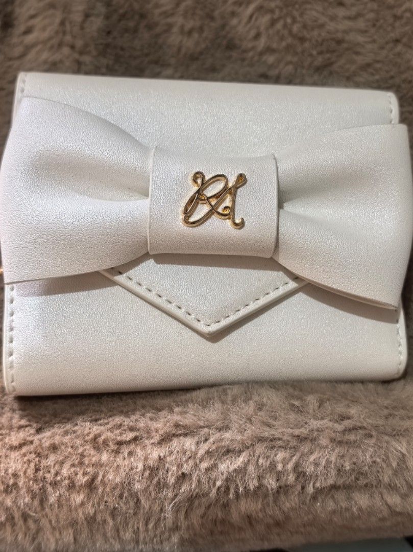 White bow wallet with gold hardware (Category: Wallets & Card holders) located in Rizal. Submitted by gkstcenit (Listing ID 1470797776, Image 1). Description: - Color: Cream white - Design: Elegant front bow with gold-tone logo monogram - Interior: Multiple card slots and a zipped coin pocket - Quality: Clean edge stitching - Size: Compact, fits easily in everyday bags.