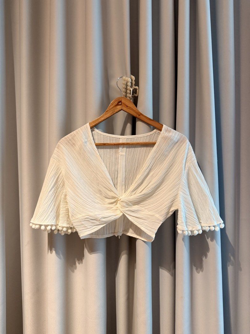 White Crop Too With Twist Front Beach Top Summer (Category: Blouses) located in Taguig. Submitted by regalbbb (Listing ID 1470754043, Image 1). Description: RFS: Decluttering Condition: Tried on once and never used - Color: White with subtle texture - Design: V-neckline with trendy front twist detail - Sleeves: Short flared sleeves with cute pom pom trim - Closure: Convenient back zipper - Fabric: Lightweight and breathable, ideal for PH weather 