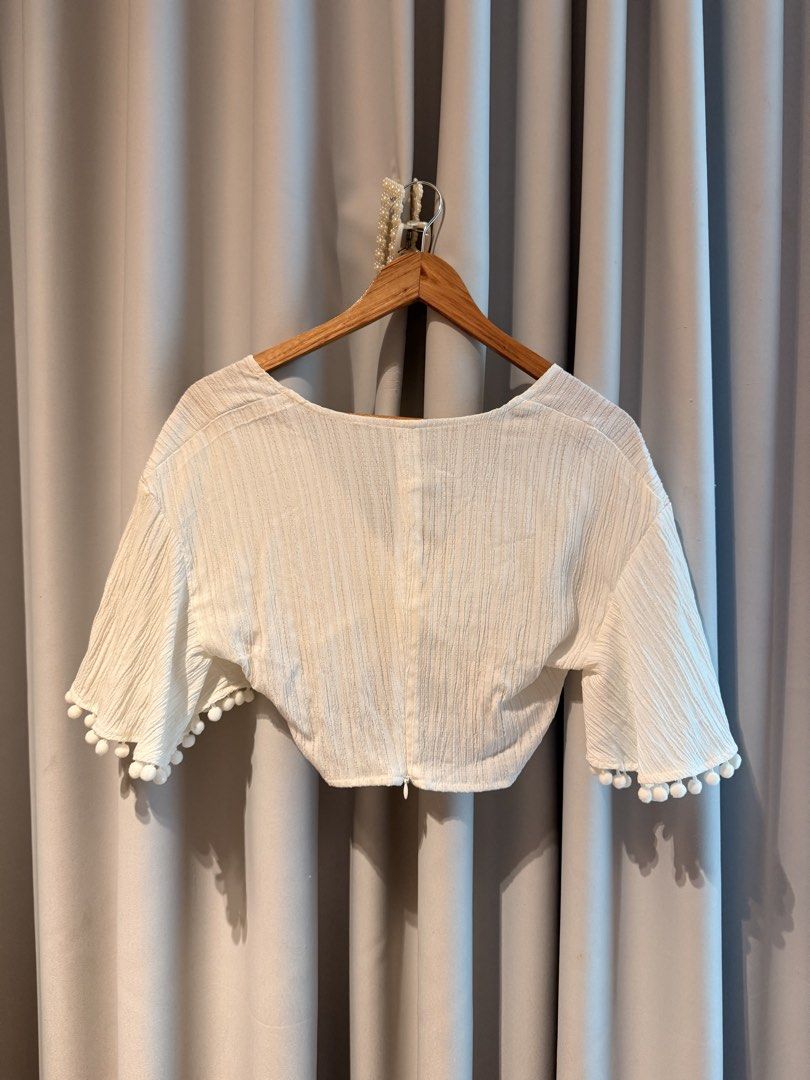 White Crop Too With Twist Front Beach Top Summer (Category: Blouses) located in Taguig. Submitted by regalbbb (Listing ID 1470754043, Image 2). Description: RFS: Decluttering Condition: Tried on once and never used - Color: White with subtle texture - Design: V-neckline with trendy front twist detail - Sleeves: Short flared sleeves with cute pom pom trim - Closure: Convenient back zipper - Fabric: Lightweight and breathable, ideal for PH weather 