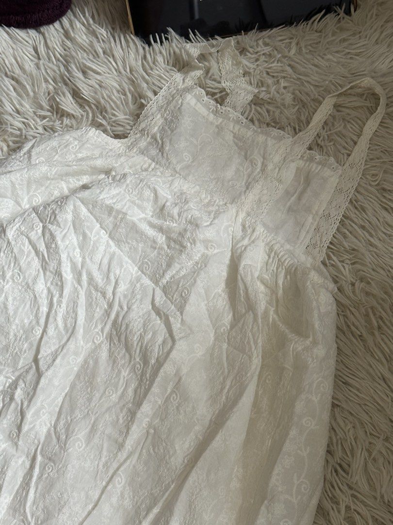 White lace trim tank top with buttons (Category: Sleeveless) located in Taguig. Submitted by appatheseller (Listing ID 1470845686, Image 3). Description: Small stain on chest area not visible - Color: White - Style: Sleeveless top with delicate lace trim along the neckline and straps - Details: Front row of small white buttons, textured fabric with subtle pattern - Fit: Elastic gathering under the chest area for a flattering silhouette - Material