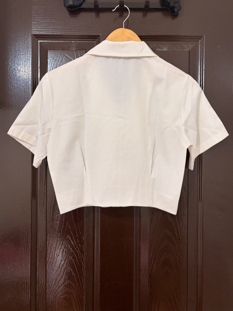 White Short Sleeve Cropped Button Up Shirt (Category: Shirts) located in Marikina City. Submitted by _bananahanaa (Listing ID 1470769677, Image 2). Description: - Color: Classic white cream - Fit: Cropped and flattering - Design: Short sleeves, lapel collar, 4 front buttons - Back details: Plain with vertical dart seams for a tailored look - Style: Clean and minimalist - fits xs-small adult.
