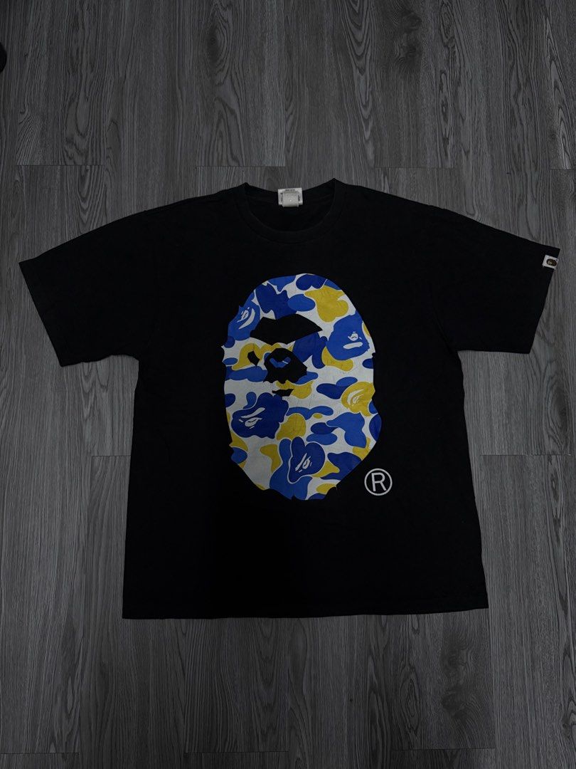 A Bathing Ape BAPE Camo Ape Head Tee (Category: Tshirts & Polo Shirts ) located in Manila. Submitted by yourfavoriteplug (Listing ID 1471054998, Image 1). Description: - Brand: BAPE (A Bathing Ape) - Item: Classic Camo Ape Head T-Shirt - Color: Black with blue, yellow, and white graphic - Size: Large - Material: 100% Cotton - Origin: Made in Japan - Condition: Good, with minor cracking on the front print (see close-up) - Details: Sleeve tag attac