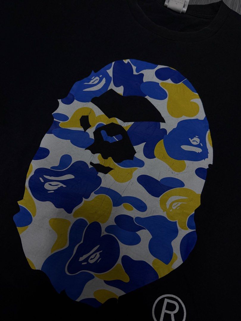 A Bathing Ape BAPE Camo Ape Head Tee (Category: Tshirts & Polo Shirts ) located in Manila. Submitted by yourfavoriteplug (Listing ID 1471054998, Image 2). Description: - Brand: BAPE (A Bathing Ape) - Item: Classic Camo Ape Head T-Shirt - Color: Black with blue, yellow, and white graphic - Size: Large - Material: 100% Cotton - Origin: Made in Japan - Condition: Good, with minor cracking on the front print (see close-up) - Details: Sleeve tag attac
