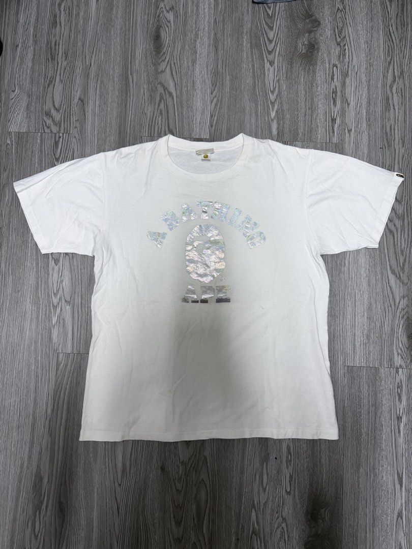 A Bathing Ape BAPE Metallic Foil Logo Tee (Category: Tshirts & Polo Shirts ) located in Manila. Submitted by yourfavoriteplug (Listing ID 1471055100, Image 1). Description: - Brand: A Bathing Ape (BAPE) - Color: White - Design: Classic Ape Head logo with shiny foil texture and bold framing text - Fit: Normal fit, short sleeves, crew neck - Condition: Regular wear visible on the collar tag and fabric - 100% authentic streetwear staple.