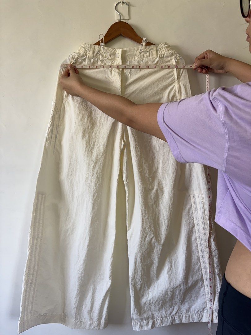 Adidas White Nylon Track Pants Size M (Category: Other Bottoms) located in Muntinlupa City. Submitted by shopkidsandmom.ph (Listing ID 1471035904, Image 3). Description: - Brand: Adidas - Color: White - Material: 100% recycled polyamide (lightweight parachute style) - Fit: Relaxed wide-leg - Waistband: Elastic with adjustable pull cords - Details: Iconic three stripes on sides, small trefoil logo near pocket - Origin: Made in China - Condition: E
