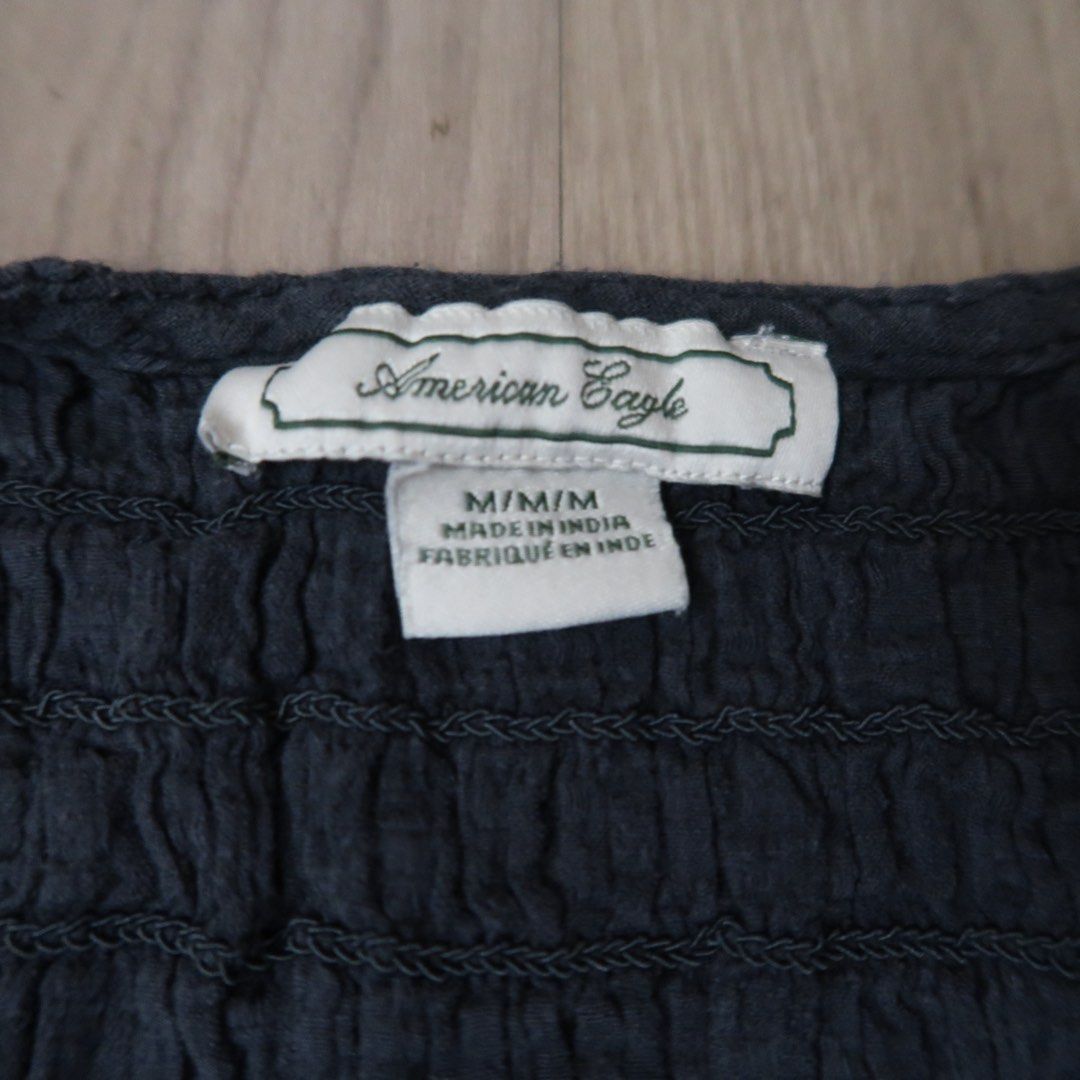 American Eagle Smocked Peplum Top Dark Gray Size M (Category: Sleeveless) located in Manila. Submitted by mixi_lexi (Listing ID 1471038292, Image 2). Description: - Brand: American Eagle - Size: Medium - Color: Dark gray - Design: Smocked bodice, deep V-neckline, short cap sleeves, and flowy peplum hem - Material: Lightweight fabric with a crinkled texture (Made in India) - Condition/Style: Easy to dress up or down for casual or formal looks.