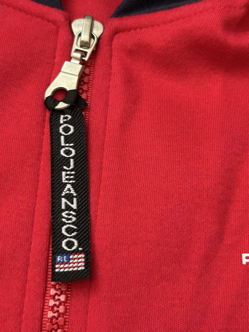Auth Polo Jeans Ralph Lauren Zip Up Jacket (Category: Coats, Jackets and Outerwear) located in Paranaque City. Submitted by madenise_declutter (Listing ID 1470976956, Image 2). Description: Vibrant red zip-up hoodie from Polo Jeans Co. Ralph Lauren. Navy blue contrast panels on the hood and sides. American flag graphic printed on the chest with Polo Jeans Co. and Ralph Lauren branding. Custom branded zipper pull tab with miniature flag detail. In