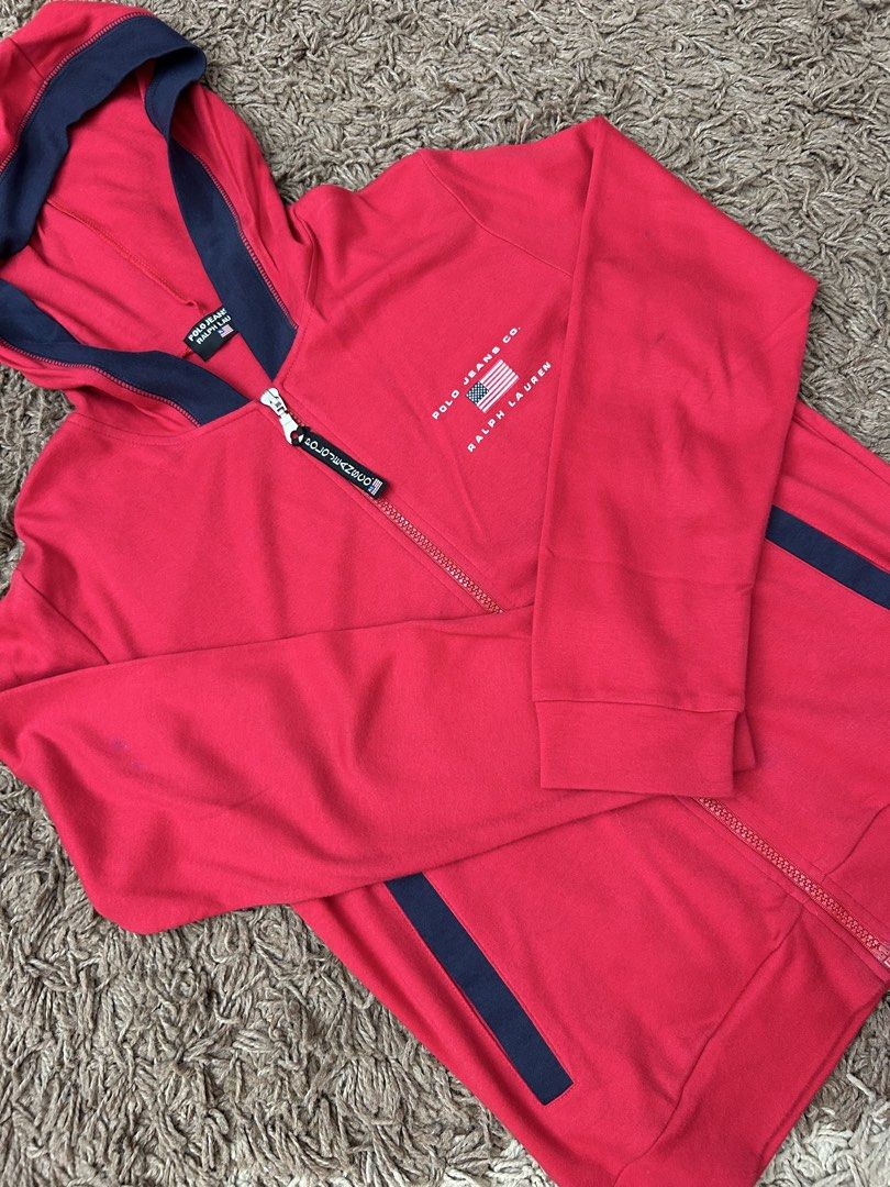 Auth Polo Jeans Ralph Lauren Zip Up Jacket (Category: Coats, Jackets and Outerwear) located in Paranaque City. Submitted by madenise_declutter (Listing ID 1470976956, Image 1). Description: Vibrant red zip-up hoodie from Polo Jeans Co. Ralph Lauren. Navy blue contrast panels on the hood and sides. American flag graphic printed on the chest with Polo Jeans Co. and Ralph Lauren branding. Custom branded zipper pull tab with miniature flag detail. In