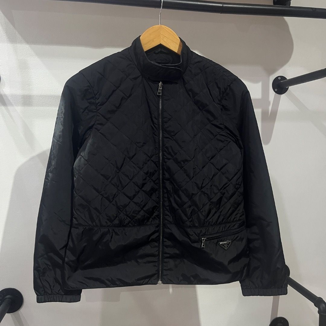 Authentic Prada Black Emblem Quilted Nylon Zip Up Jacket (Category: Coats, Jackets and Outerwear) located in Caloocan City. Submitted by achilles_grails (Listing ID 1471028486, Image 1). Description: - Brand: Prada - Item: Black quilted nylon jacket - Size: 40 - Details: Full zip front, stand collar, ribbed cuffs and hem - Feature: Lower front zipper pocket with classic Prada triangular metal logo plaque - Authenticity: Includes interior brand la