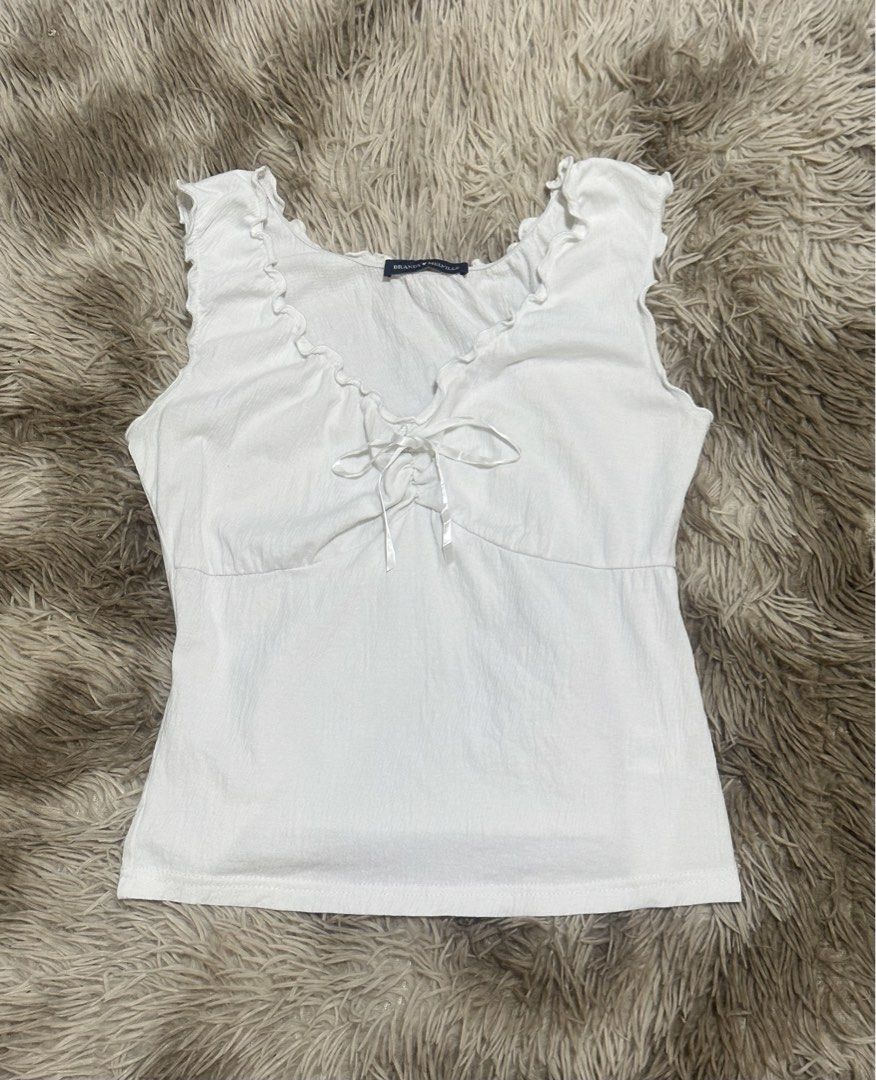Brandy Melville White Ruffle Tie-Front Tank Top (Category: Sleeveless) located in General Santos City (Dadiangas). Submitted by darylvoid (Listing ID 1470993316, Image 1). Description: - Brand: Brandy Melville - Color: White - Style Code: MH506A-Z368S - Material: 55% cotton, 42% polyamide, 3% spandex - Features: Sweetheart neckline, front tie detail, and ruffle trim - Fabric: Lightweight with a crinkled texture - Condition: Great basic piece for 