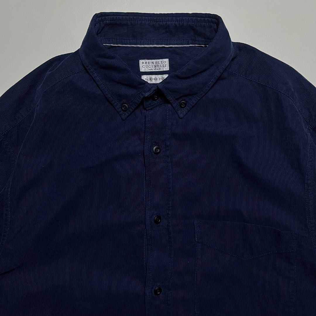 Brunello Cucinelli Dark Blue Corduroy Button-Down Shirt (Category: Tshirts & Polo Shirts ) located in Caloocan City. Submitted by achilles_grails (Listing ID 1471054652, Image 2). Description: - Brand: Brunello Cucinelli - Color: Dark blue - Material: 100% cotton with soft ribbed corduroy texture - Fit: Loose fit silhouette - Details: Button-down collar, single chest pocket, contrasting dark buttons, standard front button closure - Origin: Crafte