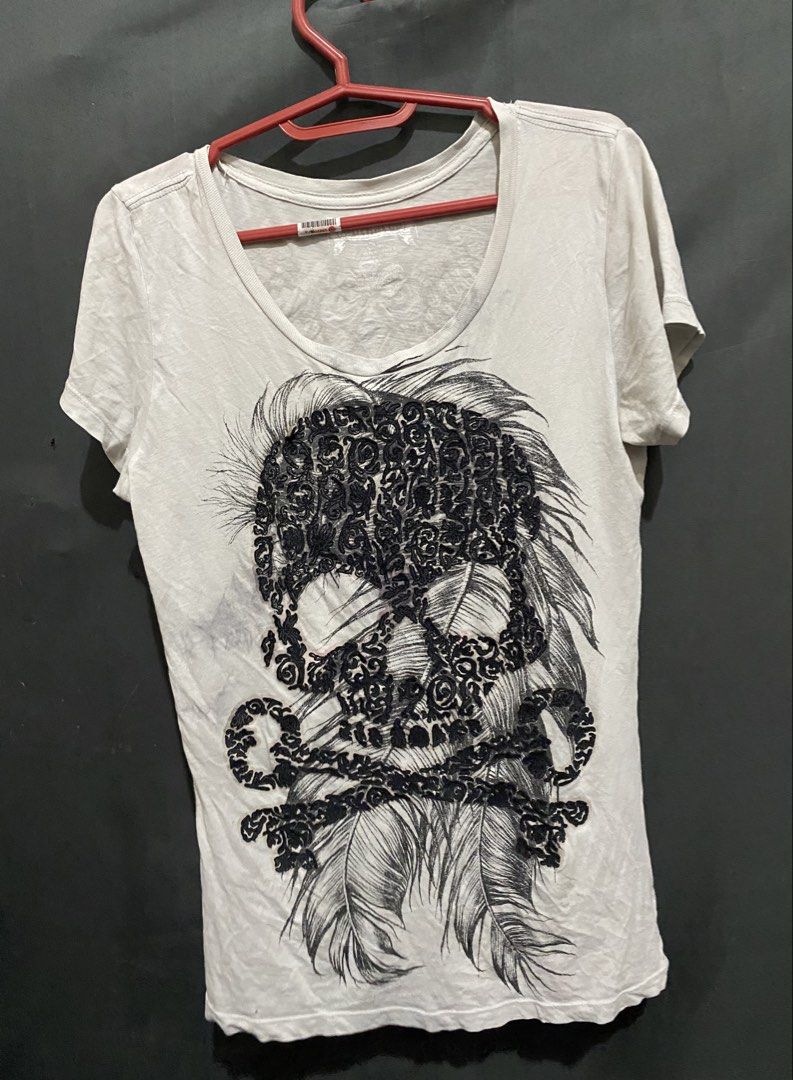 Buckaroo Skull Feather Graphic T-shirt Size S (Category: Tshirts & Polo Shirts ) located in Caloocan City. Submitted by cleverwater.ba6482 (Listing ID 1471019593, Image 1). Description: - Brand: Buckaroo - Color: Off-white - Size: S (inner collar label) - Material: 100% cotton (Made in Indonesia) - Design: Large detailed front skull graphic with black swirls and feathers; back features a winged graphic with a cross and script logo - Fit: Short sl