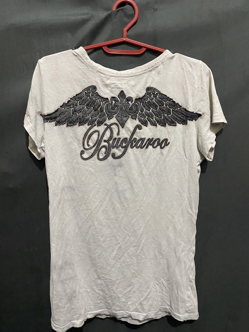 Buckaroo Skull Feather Graphic T-shirt Size S (Category: Tshirts & Polo Shirts ) located in Caloocan City. Submitted by cleverwater.ba6482 (Listing ID 1471019593, Image 3). Description: - Brand: Buckaroo - Color: Off-white - Size: S (inner collar label) - Material: 100% cotton (Made in Indonesia) - Design: Large detailed front skull graphic with black swirls and feathers; back features a winged graphic with a cross and script logo - Fit: Short sl