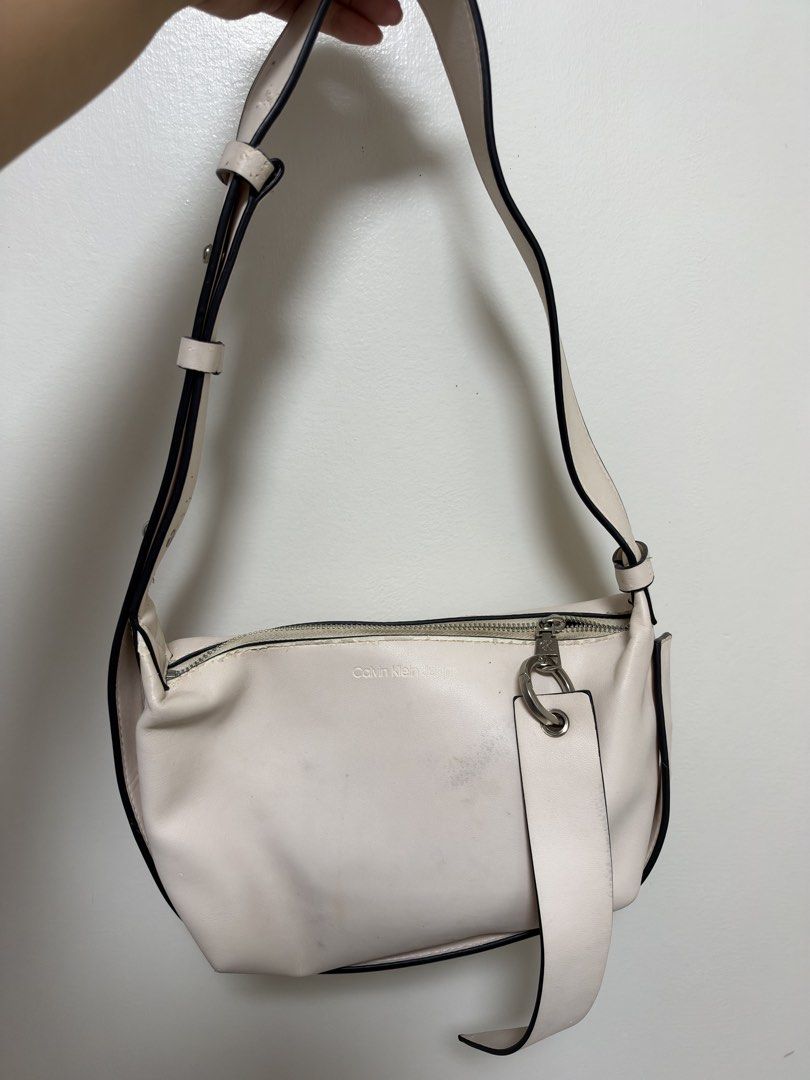 Calvin Klein Jeans Off-White Shoulder Bag (Category: Shoulder Bags) located in Manila. Submitted by cat-d526 (Listing ID 1470984364, Image 2). Description: - Brand: Calvin Klein Jeans - Color: Off-white - Closure: Zip top with silver-tone hardware and branded pull - Strap: Adjustable with buckle details - Logo: Debossed Calvin Klein Jeans logo on the front - Condition: Has noticeable scuffs and marks on the body and near the zipper area (priced a