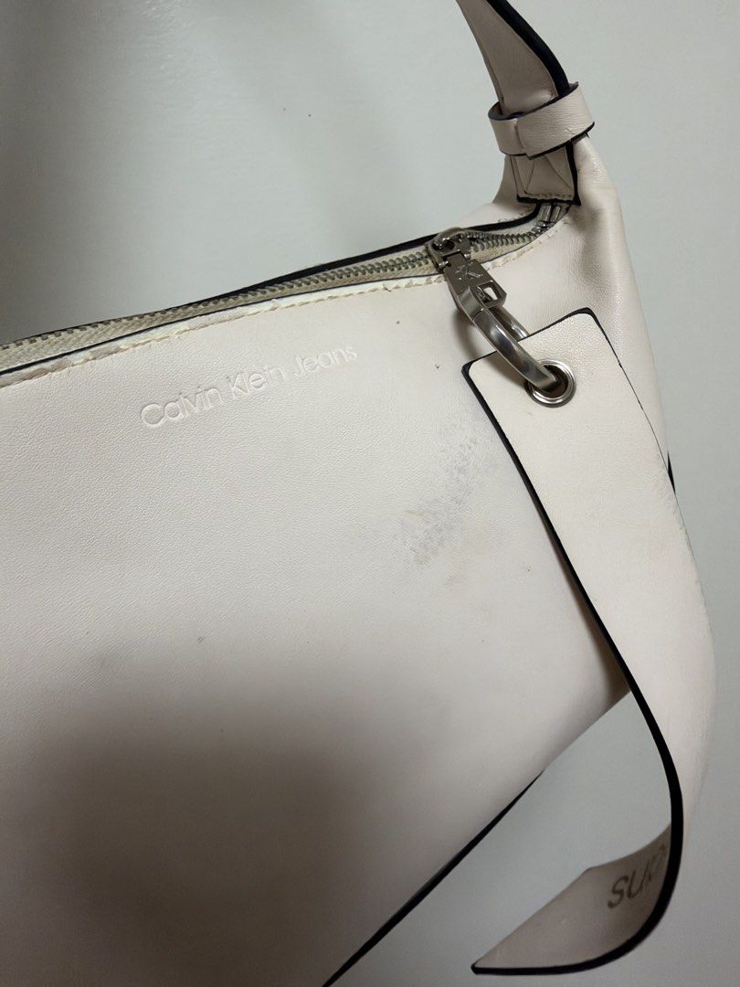 Calvin Klein Jeans Off-White Shoulder Bag (Category: Shoulder Bags) located in Manila. Submitted by cat-d526 (Listing ID 1470984364, Image 3). Description: - Brand: Calvin Klein Jeans - Color: Off-white - Closure: Zip top with silver-tone hardware and branded pull - Strap: Adjustable with buckle details - Logo: Debossed Calvin Klein Jeans logo on the front - Condition: Has noticeable scuffs and marks on the body and near the zipper area (priced a