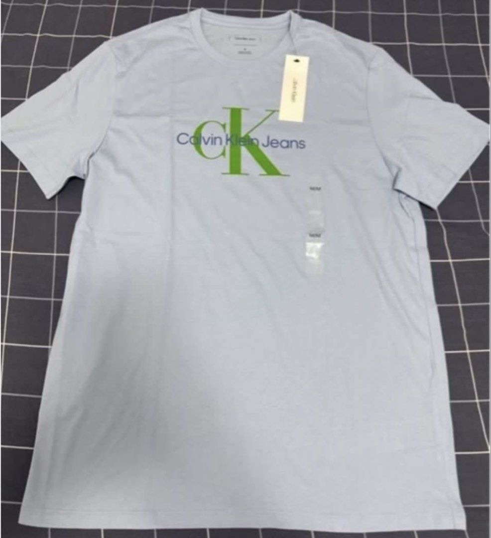 Calvin Klein Jeans T-Shirt Light Blue Medium (Category: Tshirts & Polo Shirts ) located in Pasay City. Submitted by szepter (Listing ID 1470951640, Image 3). Description: - Brand: Calvin Klein Jeans - Condition: Brand new with tags (BNWT), never worn - Size: Medium - Color: Light blue with large green and navy chest logo - Material: Soft cotton - Style: Classic crew neck, casual everyday wear - Note: Pit-to-pit measurement available in photos.