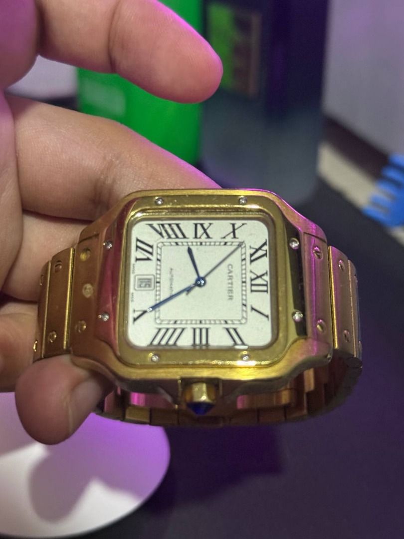 Cartier Santos Automatic Gold Watch (Category: Luxury Watches) located in Binan City. Submitted by calvin654132317 (Listing ID 1471101793, Image 3). Description: - Authentic Gold Cartier Santos automatic watch - White dial with classic black Roman numerals and striking blue hands - Date window conveniently located at the 6 o'clock position - Signature blue cabochon stone on the crown - Distinct screw details along the bezel and linked bracelet wi