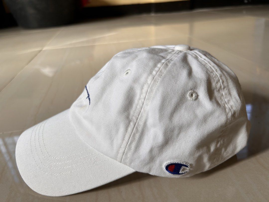 Champion - White Cap (Category: Caps & Hats) located in Caloocan City. Submitted by declutterieee (Listing ID 1471017134, Image 2). Description: - Brand: Champion - Color: White - Design: Embroidered script logo on front and small logo patch on side - Closure: Adjustable strapback with metal buckle - Style: Classic everyday staple piece - Authentic.