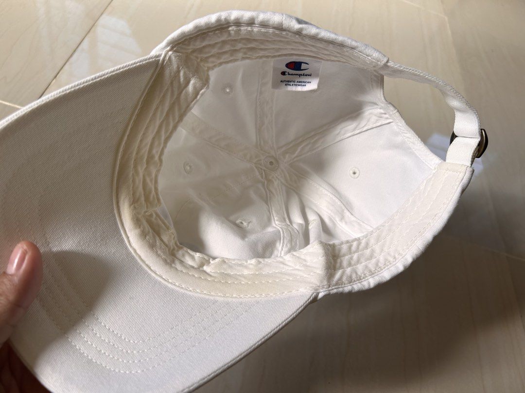 Champion - White Cap (Category: Caps & Hats) located in Caloocan City. Submitted by declutterieee (Listing ID 1471017134, Image 3). Description: - Brand: Champion - Color: White - Design: Embroidered script logo on front and small logo patch on side - Closure: Adjustable strapback with metal buckle - Style: Classic everyday staple piece - Authentic.
